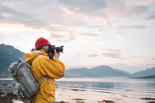 Hipster traveler photographer takes a photo beautiful nordic landscape on professional camera. Man tourist with backpack shoots a photo scandinavia nature