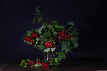 Branches of red viburnum in a glass vase stand on a table