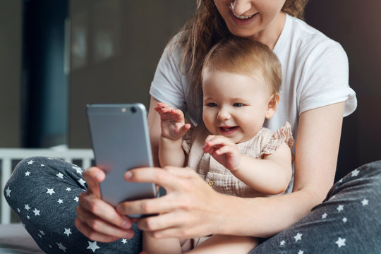 Nine-month-old baby girl sits with her mother and looks on smartphone cartoons. Child is talking to her grandmother via video link