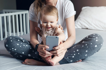 Nine-month-old baby girl sits with her mother and looks on smartphone cartoons. Child is talking to her grandmother via video link