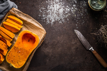 Food background with butternut pumpkin on baking sheet on dark rustic background with knife, top...