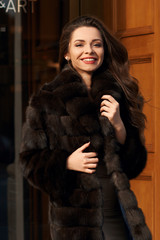 Dynamic fashion portrait of young beautiful happy woman in brown fur coat and beige dress walking...