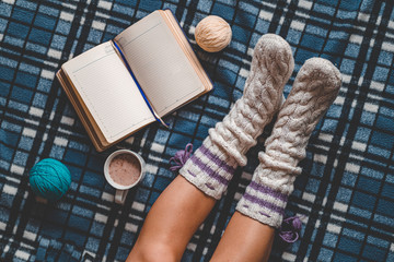 Comforting cozy woman in knitted winter white warm socks sitting on a blue checkered plaid blanket...