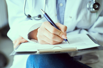 Female doctor hand hold silver pen filling patient history list at clipboard pad. Panacea and life save, prescribing treatment.