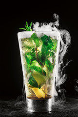 Cocktail with lemon, mint, rum and ice with smoke effect over black background closeup