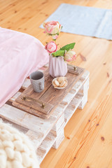 Fototapeta na wymiar Tray with a romantic breakfast and rose (tea, cakes and a bouquet of peonies) in the bedroom in pastel colors