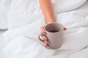 Woman hand hold cup of tea on the bed