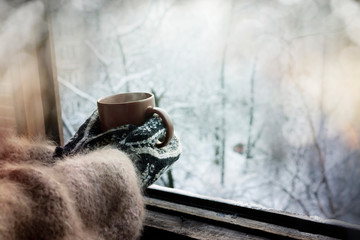 Hands in knitted mittens with  cup of hot drink on background of winter nature