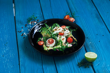 salad of arugula, avocado, cottage cheese, radish and cherry tomatoes on a black glossy plate