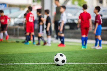 Soccer ball on green artificial turf with blurry soccer team training. Blurry kid player training and soccer equipment in soccer academy.
