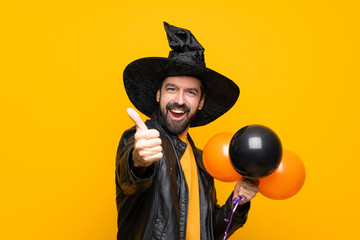 Man with witch hat holding black and orange air balloons for halloween party with thumbs up because...