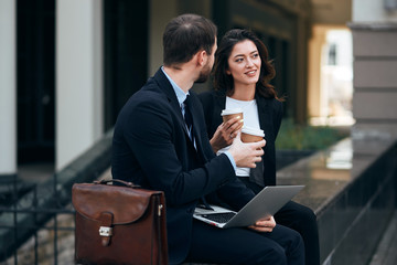 thoughtful beautiful brunette elegant woman and handsome man talking in the street, young people holding cups having pleasant conversation