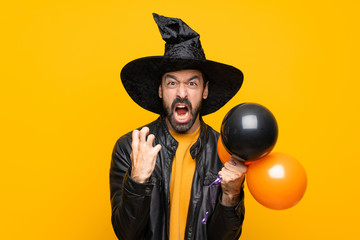 Man with witch hat holding black and orange air balloons for halloween party frustrated by a bad...