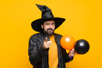 Man with witch hat holding black and orange air balloons for halloween party frustrated and...