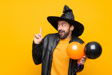 Man with witch hat holding black and orange air balloons for halloween party intending to realizes the solution while lifting a finger up