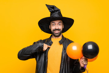 Man with witch hat holding black and orange air balloons for halloween party with surprise facial expression