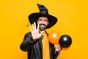 Man with witch hat holding black and orange air balloons for halloween party counting five with...