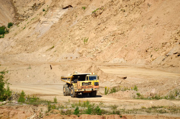 Big yellow dump truck transporting stone and gravel in an sand open-pit. Mining quarry for the production of crushed stone, sand and gravel for use in the construction industry