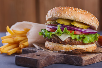 Burger with a beef, green, onion, tomato on a wooden cutting board