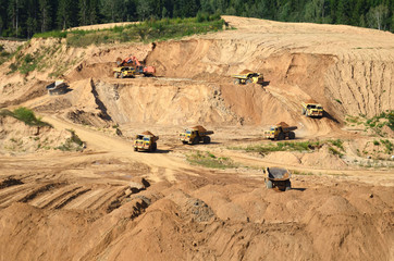 A lot of mining trucks work in an sand open pit .Dump truck transporting stone and gravel . Mining quarry for the production of crushed stone, sand and gravel for use in the construction industry