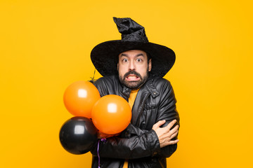 Man with witch hat holding black and orange air balloons for halloween party freezing
