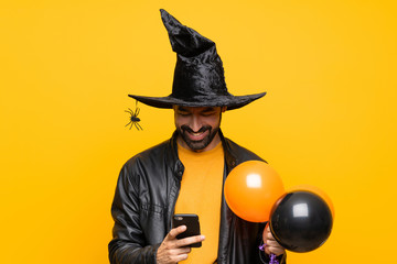 Man with witch hat holding black and orange air balloons for halloween party sending a message with...