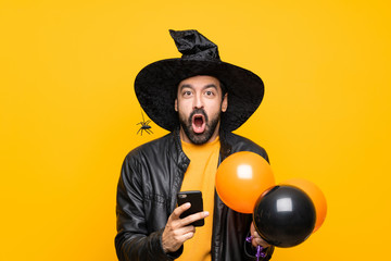 Man with witch hat holding black and orange air balloons for halloween party surprised and sending...