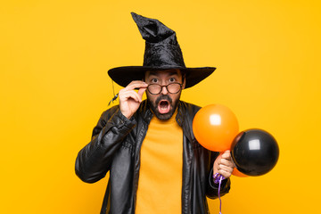 Man with witch hat holding black and orange air balloons for halloween party with glasses and...