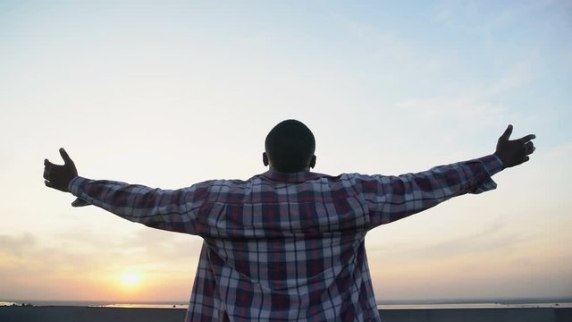 Afro-American man stretching hands on sunset background, inspiration, back-view