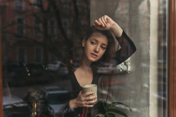 Attractive girl with long brunette hair behind the glass, coffee shop window, concept of female...