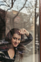 Portrait of a beautiful smiling brunette sitting in a coffee house behind a glass, a concept of femininity and natural beauty, a lifestyle