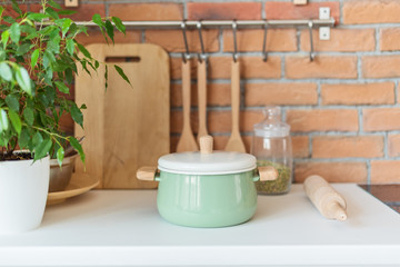 Green pot on the countertop in the kitchen in loft style over brick wall, wooden spoon, wooden paddle, wooden spork