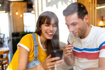 happy couple eating food and looking at mobile phone at cafe