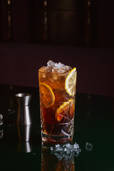 Cocktail with rum, orange and ice on black table near ice, jigger and strainer