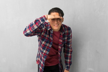 Man over grunge wall looking far away with hand to look something