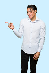 Handsome man pointing finger to the side in lateral position over isolated blue background