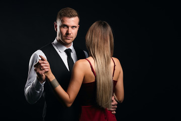 stylish fashion man holding his lady's hand looking at the camera. isolated black background, studio shot. copy space