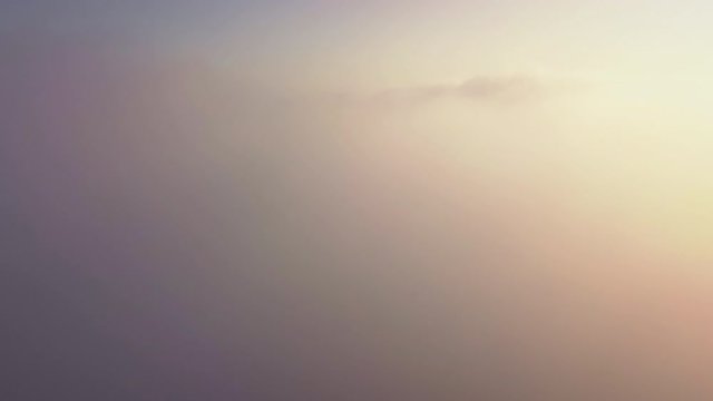 Epic aerial view from above beautiful clouds in orange morning or evening sun light. Drone flying high through fluffy rolling clouds in sky during sunrise or sunset. Cloudscape airplane window view
