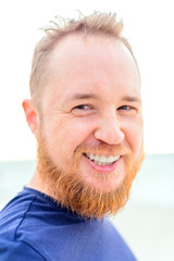 Smiling man with dark hair, red beard and freckles look at camera on the background of sea