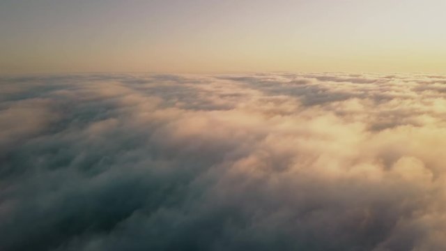 Epic aerial view from above beautiful clouds in orange morning sun light. Drone flying high over fluffy rolling clouds in sky during sunrise or sunset. Cloudscape airplane window view