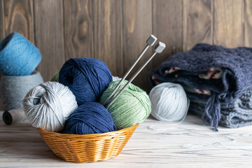 Knitting materials. Blue and green yarn in a basket with needles on wooden background
