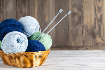Knitting blue and green yarn in a basket with needles on wooden background