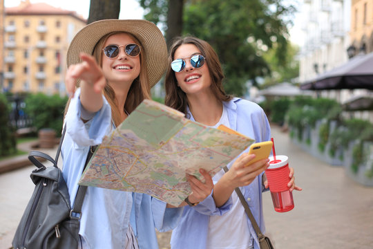 Two pretty girls dressed in summer clothes holding city map while standing outdoors.