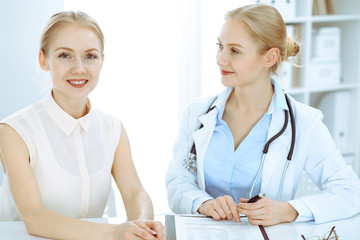 Doctor and patient talking in hospital office while sitting at the desk. Health care and client service in medicine