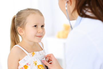 Doctor examining a little girl by stethoscope. Happy smiling child patient at usual medical inspection. Medicine and healthcare concepts