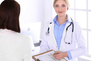 Young woman doctor and patient at medical examination at hospital office. Blue color blouse of therapist looks good. Medicine and healthcare concept