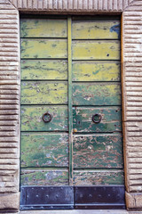 Close-up of an old entrance door with green scraped paint, rusty iron rings and stone frame, Tuscany, Italy