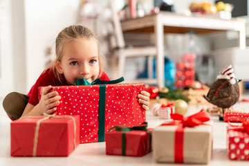 Cute excited young girl sitting on the living room floor surrounded by christmas presents, ready to open them. Happy kid at christmas with xmas gifts.