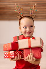 Cute young girl holding stack of christmas presents, smiling and looking away from camera. Happy kid at christmas time.