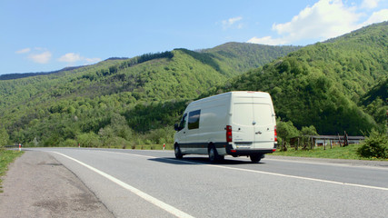 White van traveling at speed on the roads against the backdrop of mountains and pure summer sky